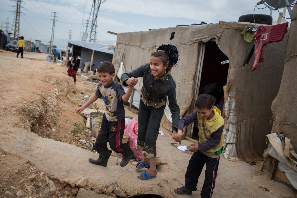 Lebanon / Syrian Refugees / Young siblings Rahaf, 12, Fady, 7, and Ali, 6, walk together between shelters outside their home in in Fayda tented settlement, in the Bekaa Valley, Lebanon, on April 17, 2014. The 3 siblings are all blind by birth and struggle with daily life in the settlement where they live. They fled here 2 years ago from Homs alongside their mother and 4 other siblings. At first it was difficult for the children to adapt to their new surroundings however now that they are familiar with their immediate environment they are able to move around within a limited area. "They taught themselves to walk around" says Fawza, their mother, "they are having difficulties here because they're not used to it, at home it was much easier for them. Rahaf broke her arm a while back and last winter Ali burnt himself with the heater." Rahaf says, "It was very hard when we first got here; we had to learn from scratch where everything is inside the house. We don't stray from the tent alone. The farthest we go is the school. One of our friends or my brother Khaled always take us but am learning the way on my own now." UNHCR / A. McConnell / April 2014